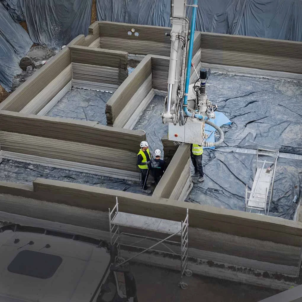Printing equipment and workers among 3D-printed concrete walls on a construction site.